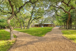 A park with a gravel path leading to a building with a covered porch. - Ultimate Riverfront Retreat! Blanco Family Cabin (Blanco)