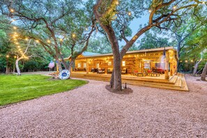 Una cabaña de madera con terraza, rodeada de árboles y luces colgantes.