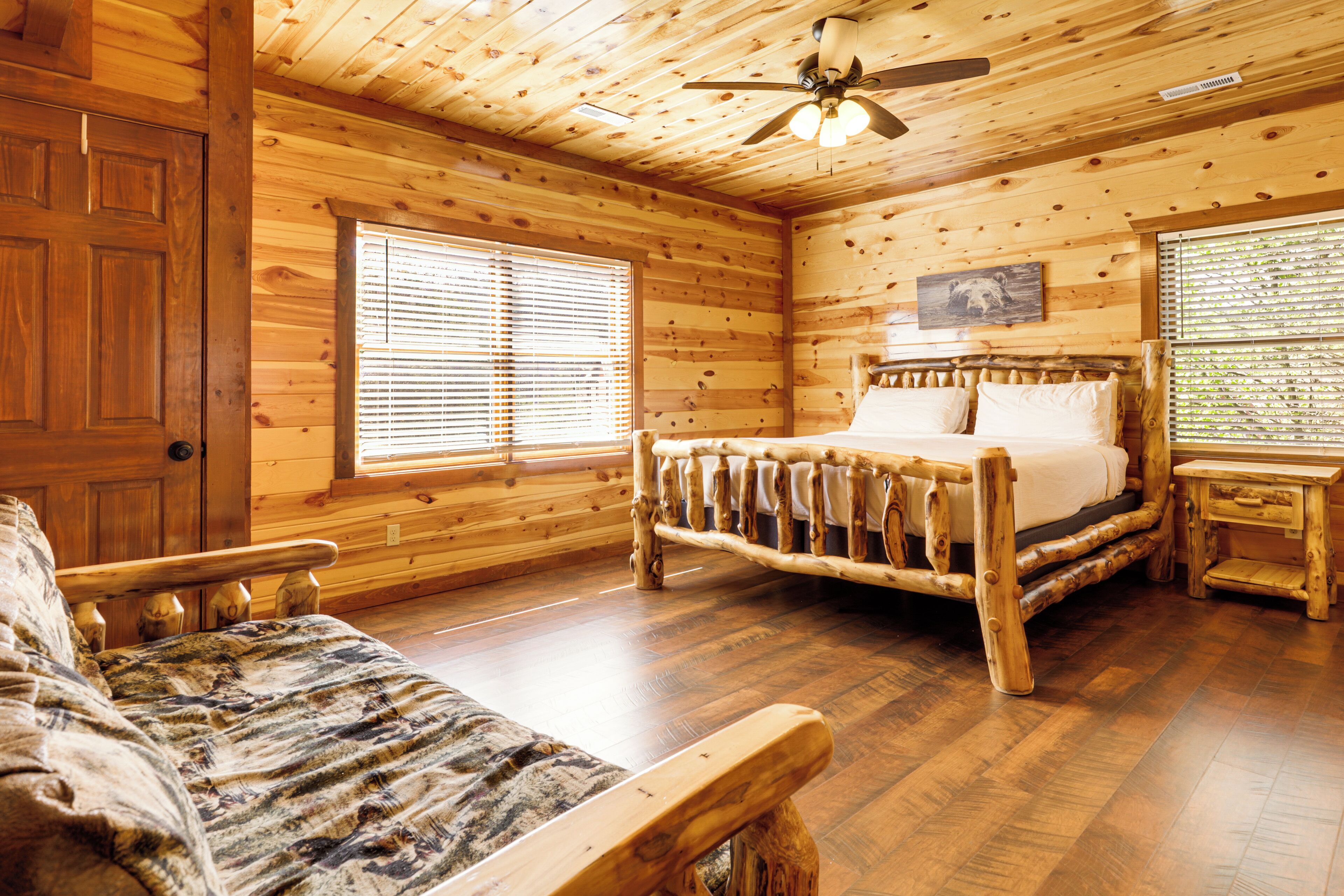 A log cabin room with a wooden bed, a wooden bench, and a ceiling fan.