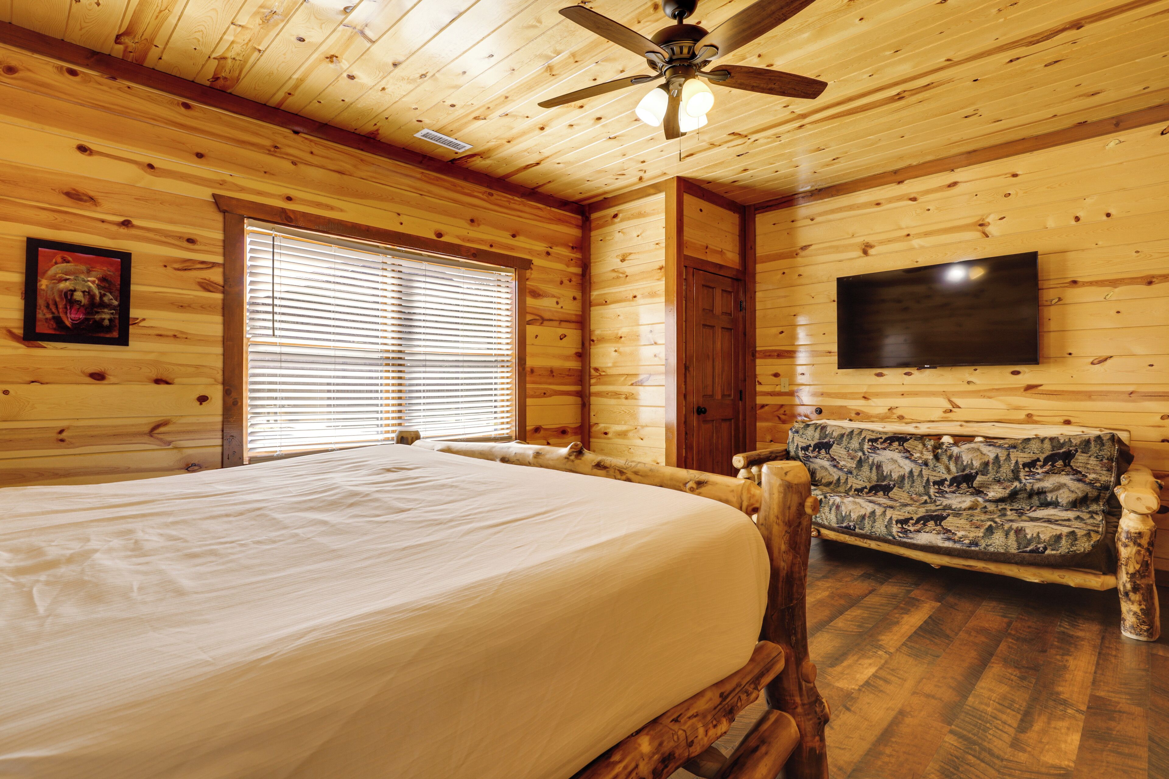 A wooden cabin room with a bed, a sofa, a ceiling fan, and a TV mounted on the wall.
