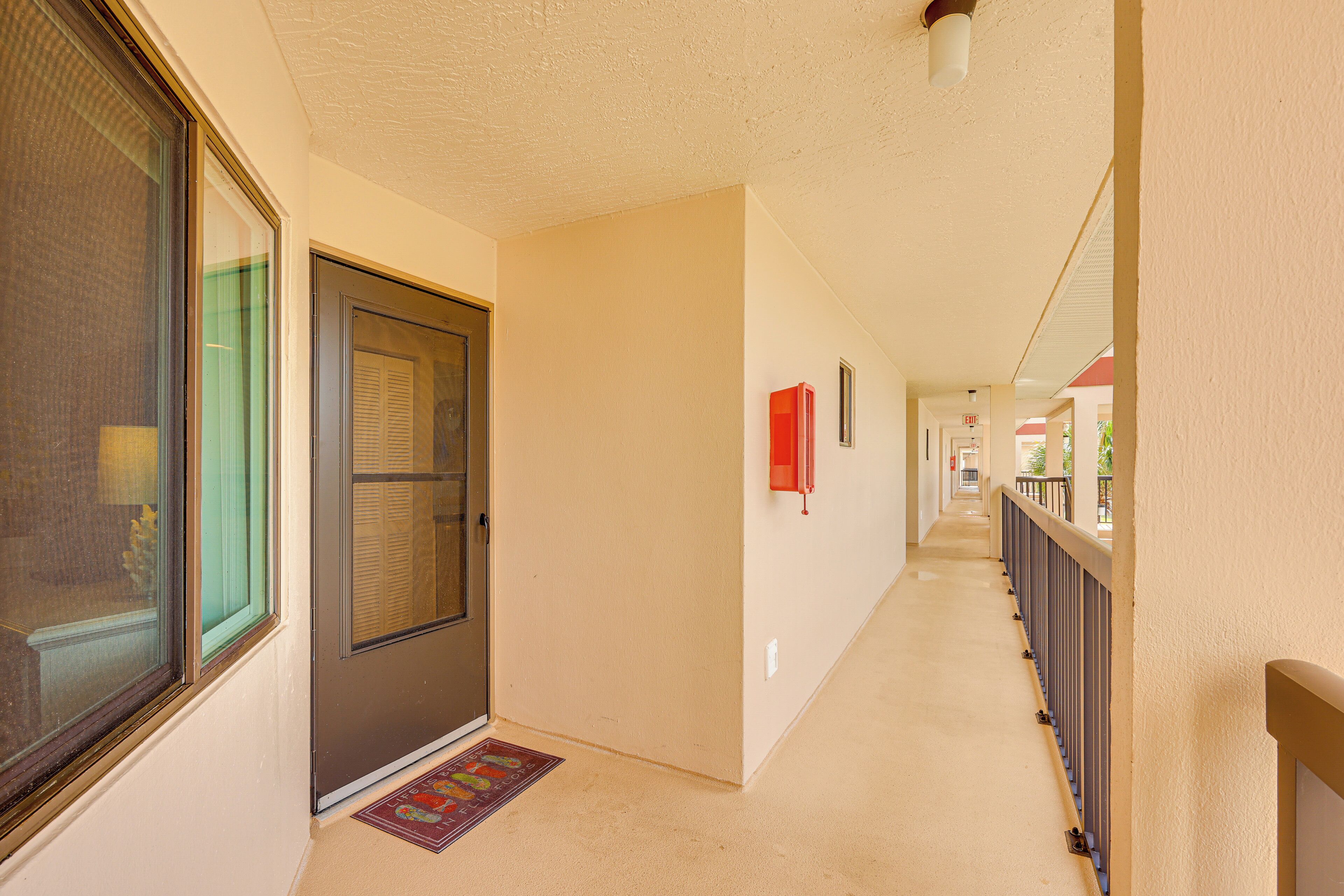 A corridor with a door, a fire alarm, and a railing.