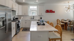 A modern kitchen with white cabinetry, a stainless steel refrigerator, a central island, and a dining area with wooden chairs.