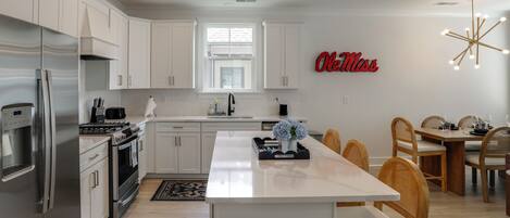 A modern kitchen with white cabinetry, a stainless steel refrigerator, a central island, and a dining area with wooden chairs.