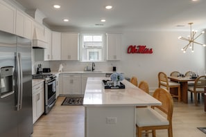 A modern kitchen with white cabinetry, a stainless steel refrigerator, a central island, and a dining area with wooden chairs.