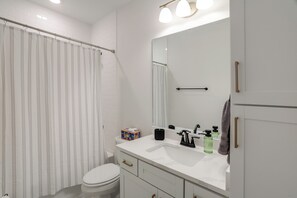 A bathroom with a white toilet, a shower curtain, a sink with a mirror, and a towel rack.
