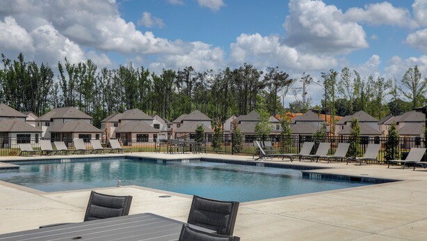 A swimming pool with lounge chairs and a table, surrounded by houses and trees.