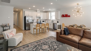 A modern kitchen with white cabinets, a central island with bar stools, a dining area with a wooden table and chairs, and a ceiling fan.