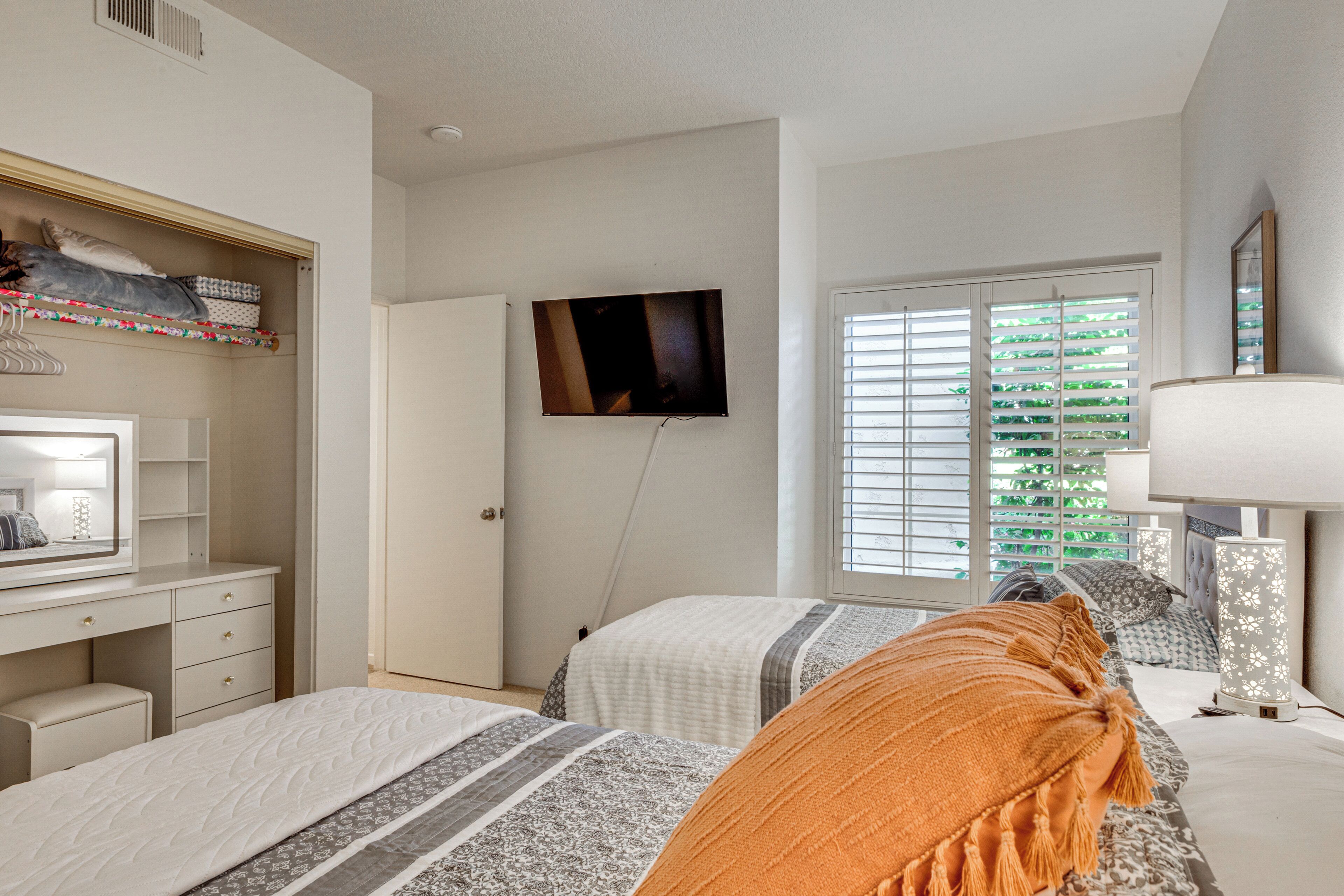 A bedroom with two beds, a TV, a desk, and a window with blinds.