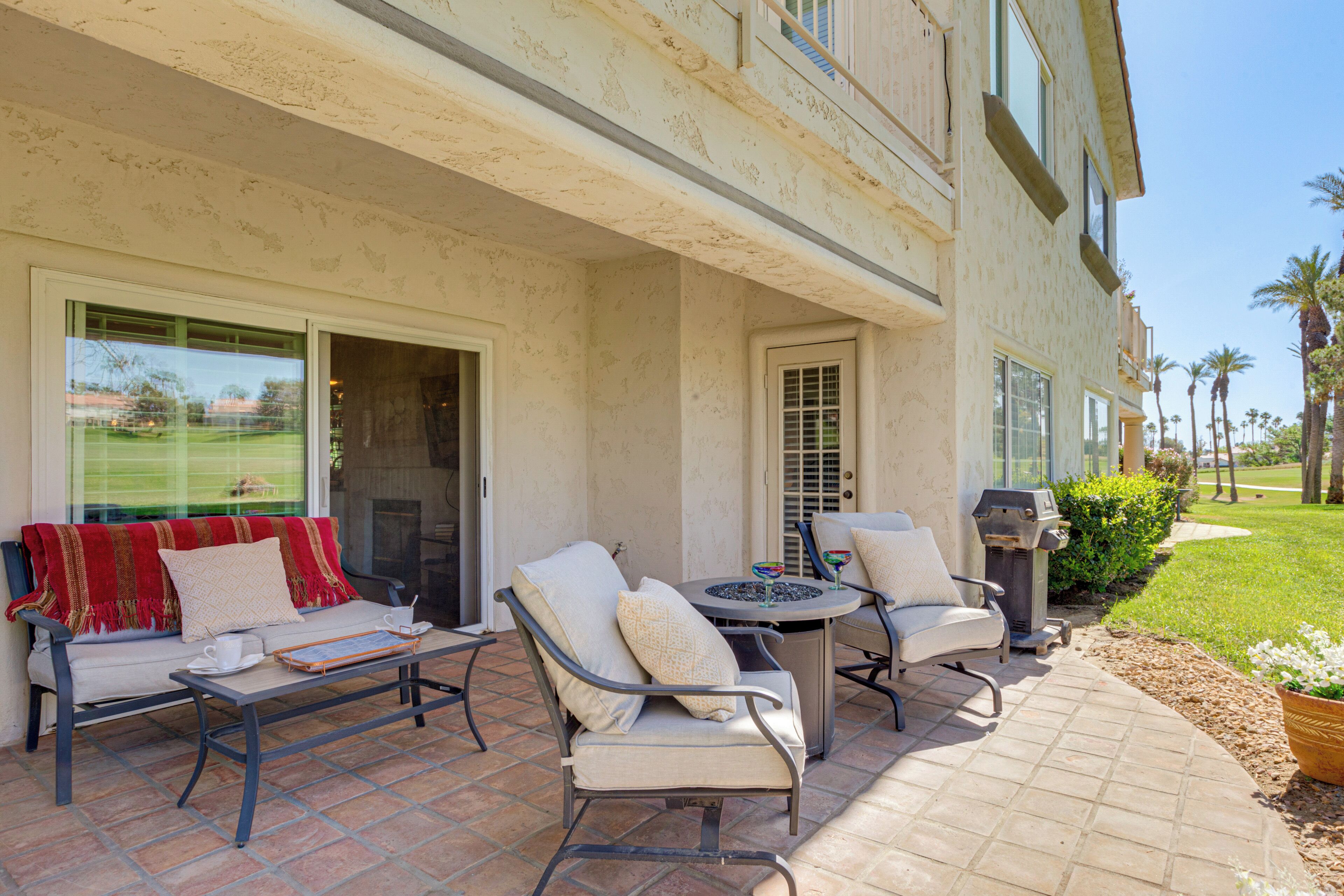 Eine Terrasse mit Gartenmöbeln, einem Grill und Blick auf einen Golfplatz.