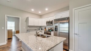 A modern kitchen with white cabinetry, stainless steel appliances, and a granite countertop island. - Walk to Cumberland County Playhouse! Modern Home (Crossville)