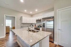 A modern kitchen with white cabinetry, stainless steel appliances, and a granite countertop island.