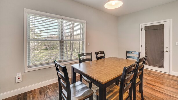 A dining area with a wooden table and chairs, a window with blinds, a door with a curtain, and a ceiling light. - Walk to Cumberland County Playhouse! Modern Home (Crossville)
