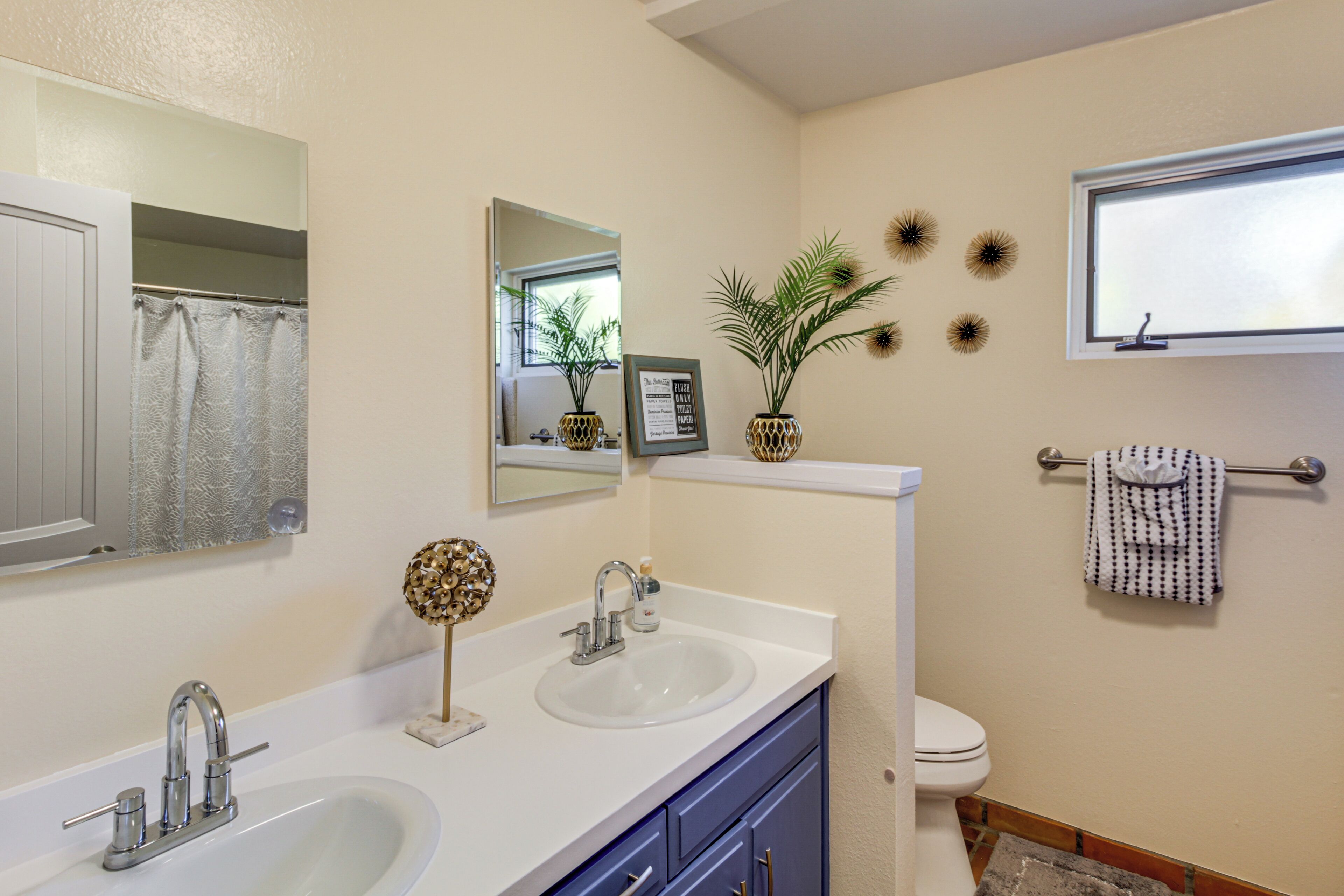 A bathroom with two sinks, a toilet, a mirror, and decorative items.