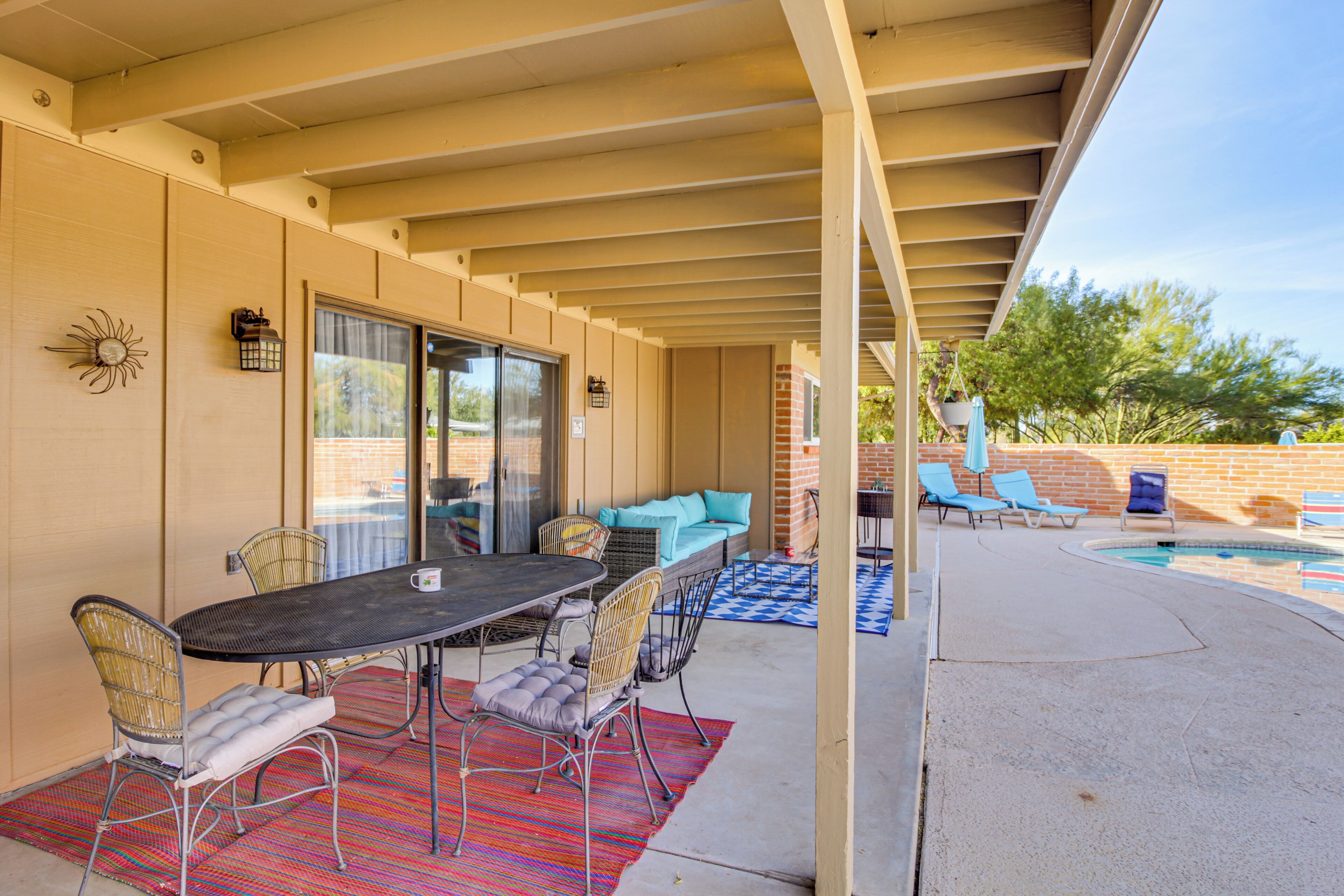A covered patio with a dining table, chairs, and a pool area.