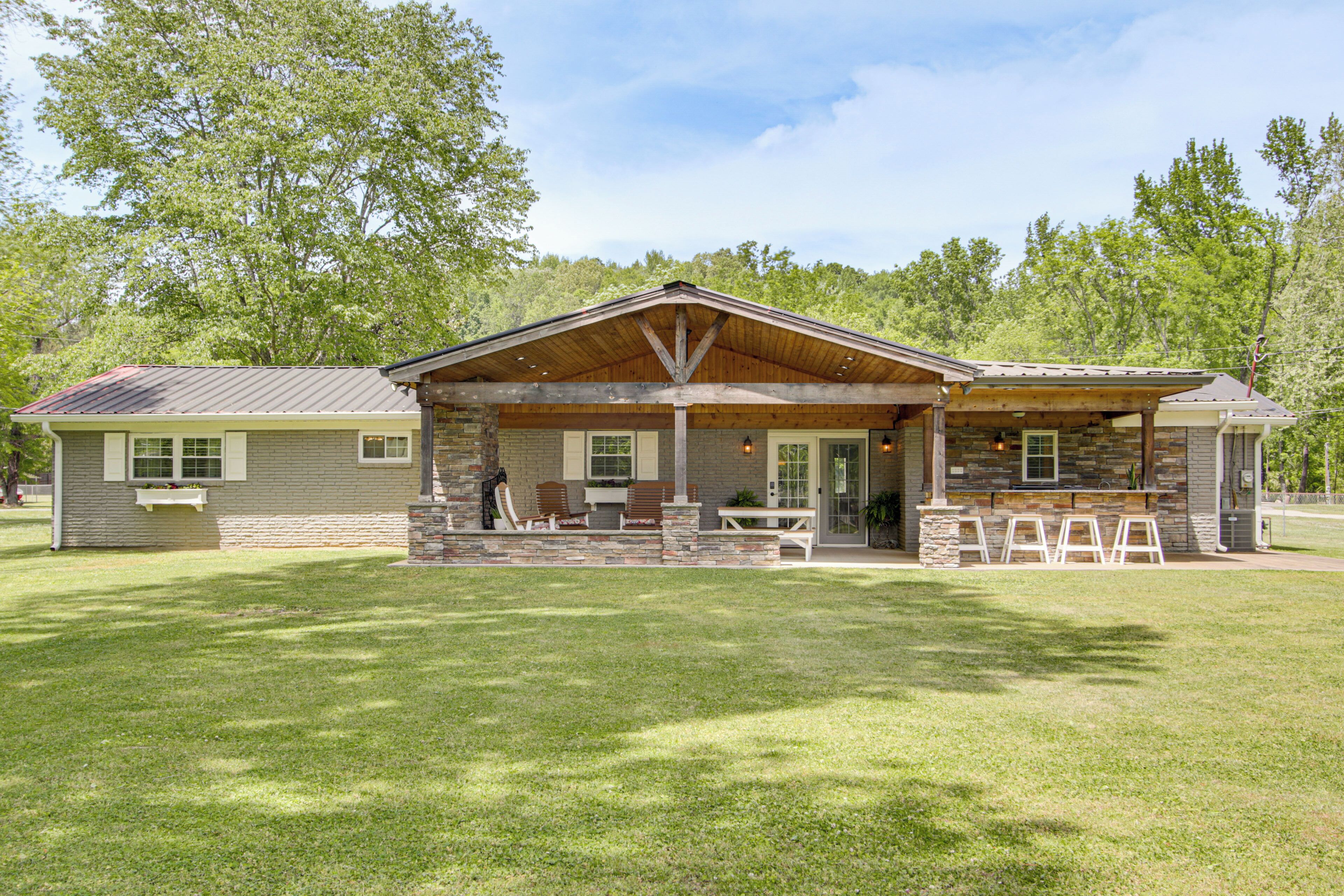 A two-story building with a covered porch, stone foundation, and a lawn in front.