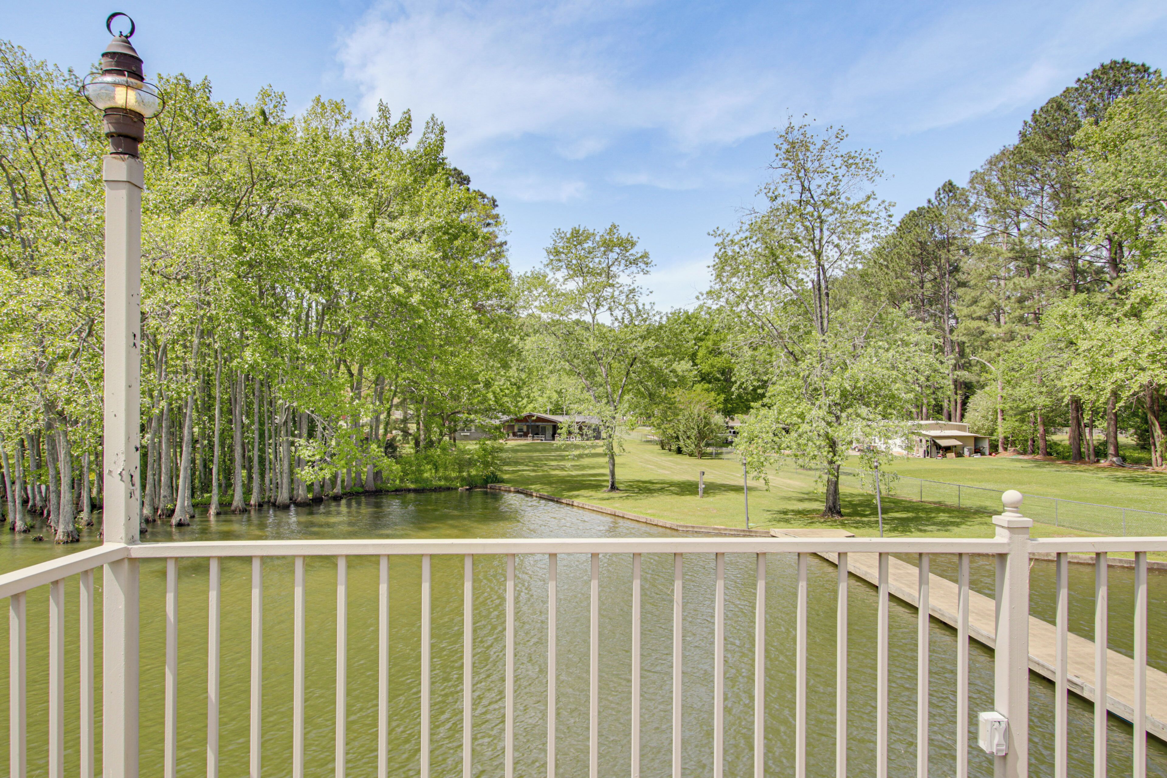 A view from a balcony with a railing, a body of water, trees, and a distant building.
