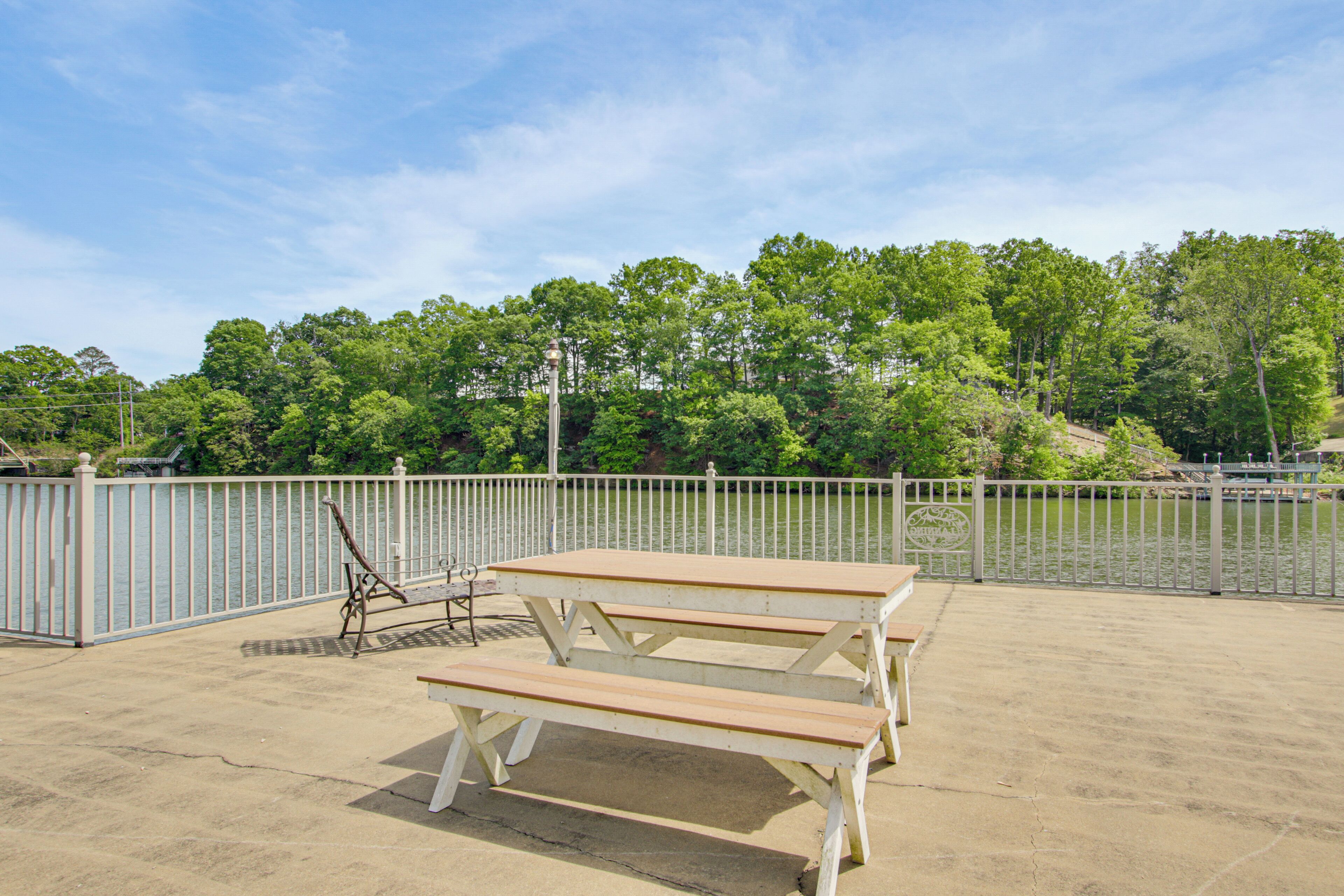 A picnic table with benches, a metal fence, and a body of water in the background.