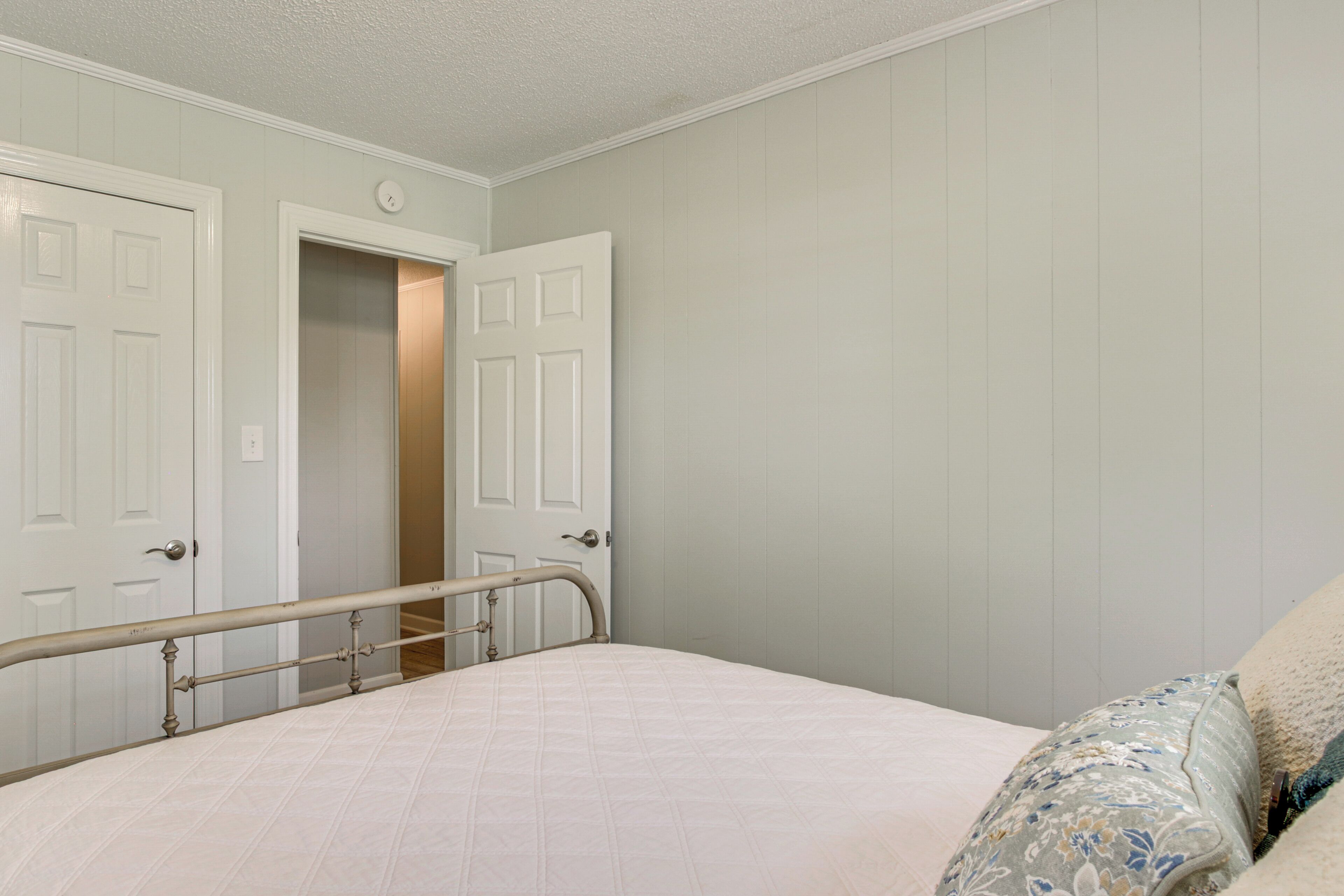A bedroom with a bed, a door, and a wall with a door frame.