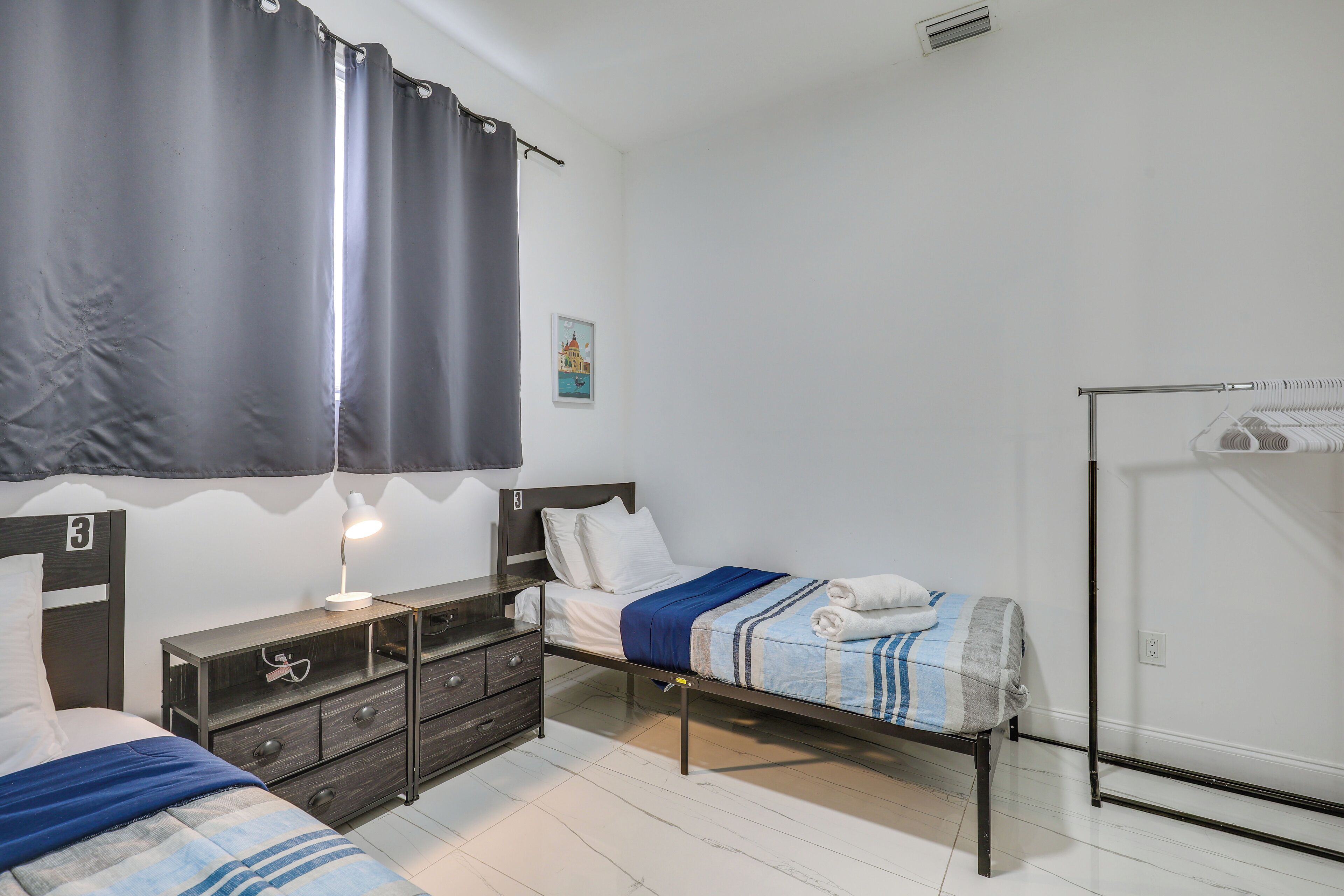 Ein Schlafzimmer mit Bett, Kommode, Nachttisch mit Lampe, Kleiderschrank und einer kleinen Wanddekoration.