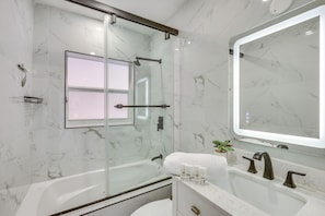 Une salle de bain moderne avec une douche Ă parois de verre, un grand miroir et un mur en marbre blanc.