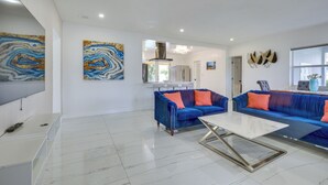 A modern living room with a TV, two blue sofas with orange cushions, a white coffee table, and abstract wall art. - Luxe Ft Lauderdale Pool Oasis Near Airport & Beach (Fort Lauderdale)