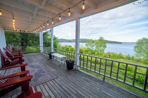 Una terraza techada con sillas de madera, una mesa y vistas a un lago.