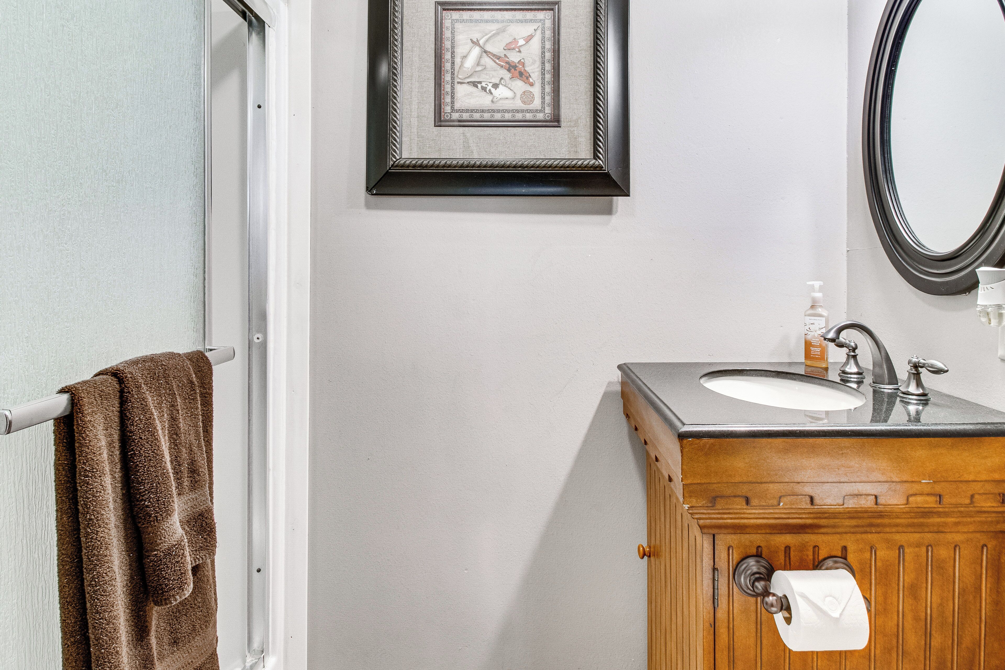 Une salle de bain avec un meuble-lavabo en bois, un évier, un miroir, un porte-serviettes et un tableau encadré au mur.