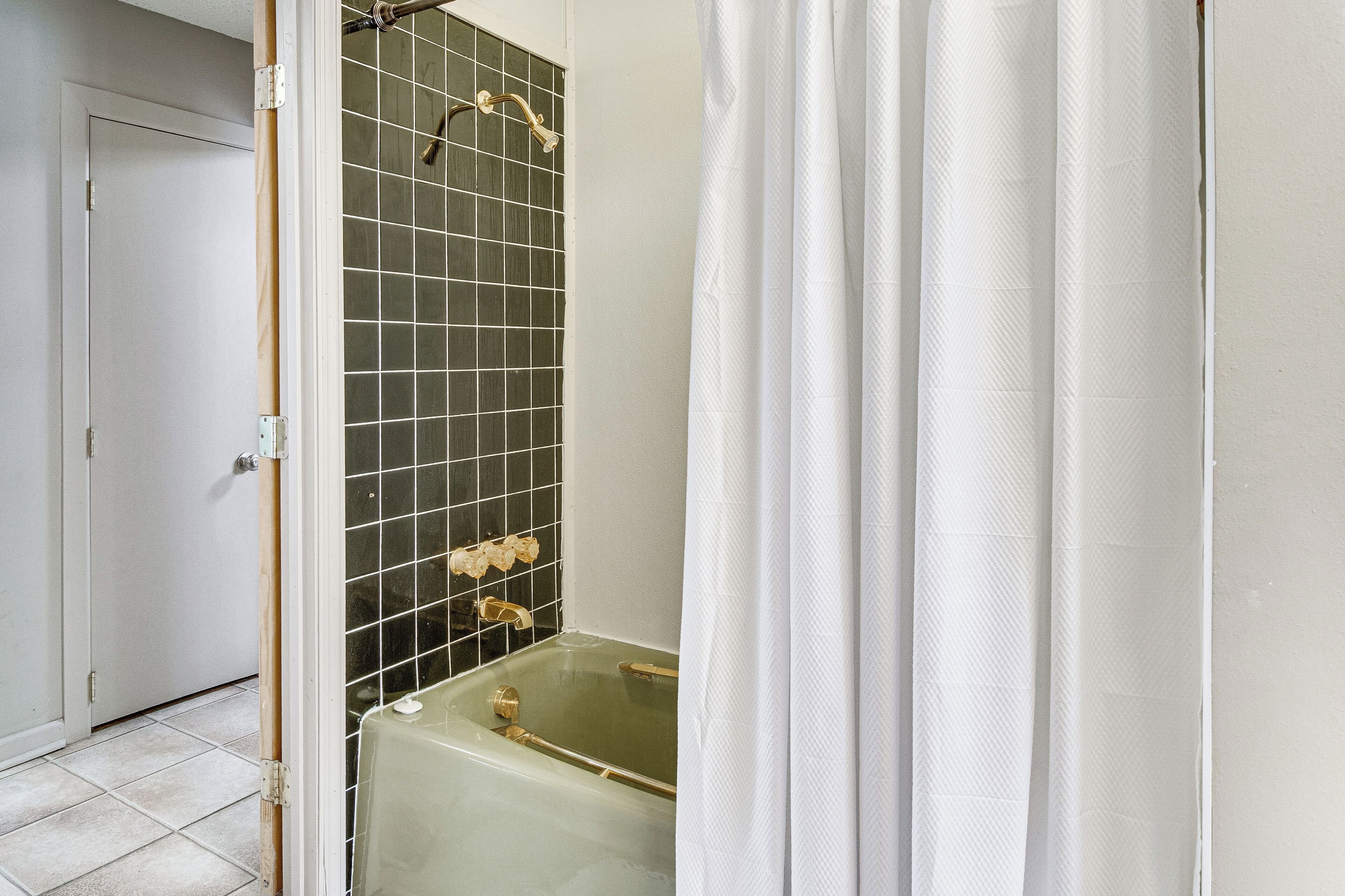 Ein Badezimmer mit Badewanne, Dusche mit gefliesten Wänden und weißem Vorhang.
