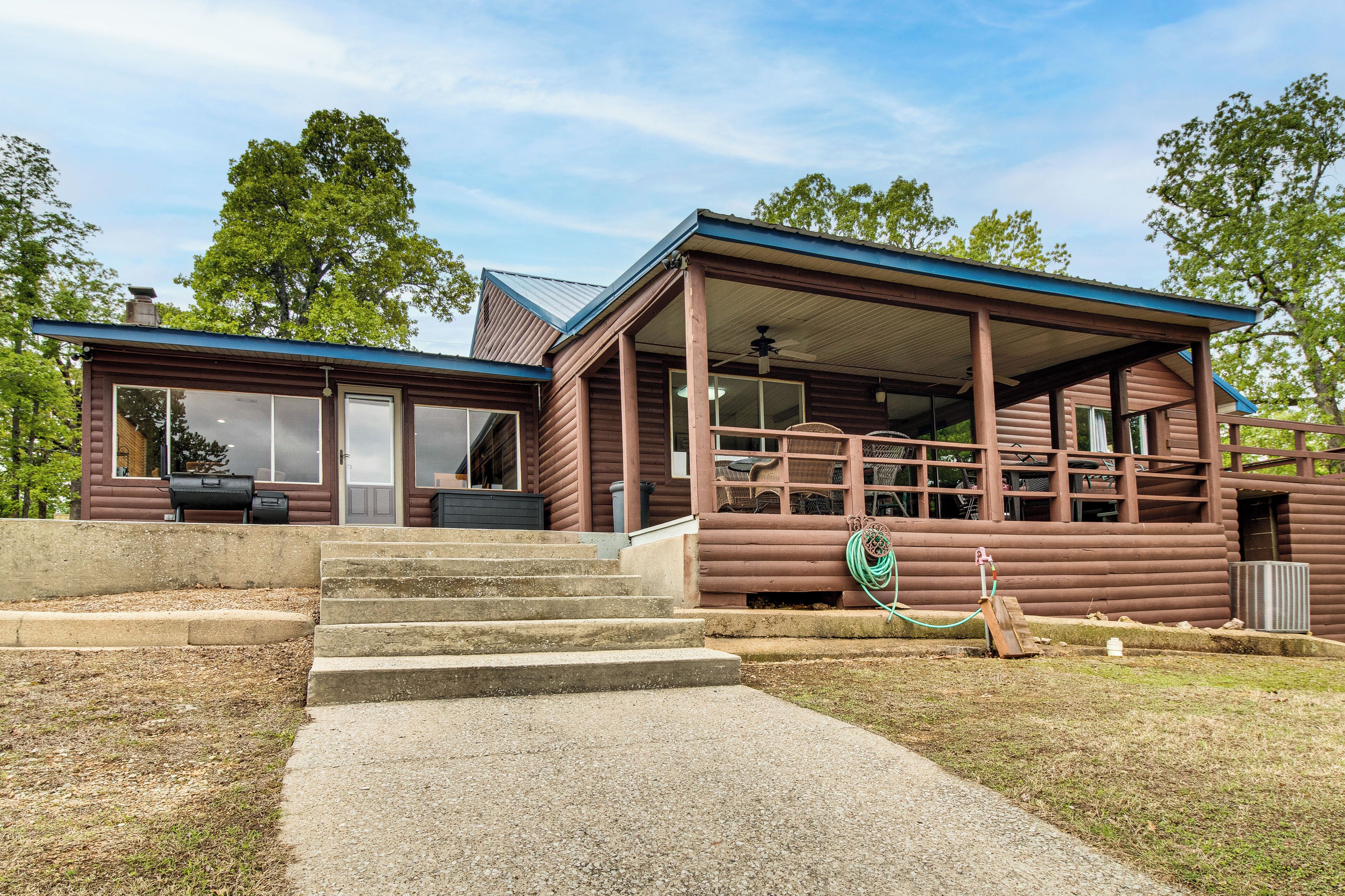 A log cabin with a porch, a covered outdoor seating area, and a visible grill.