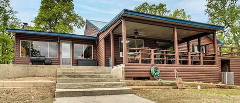 A log cabin with a porch, a covered outdoor seating area, and a visible grill.