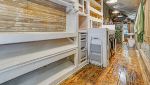 A laundry area with wooden flooring, white shelving units, and a hanging green towel. - Walk to Granbury Square & Beach! 'texas Cottage' (Granbury)