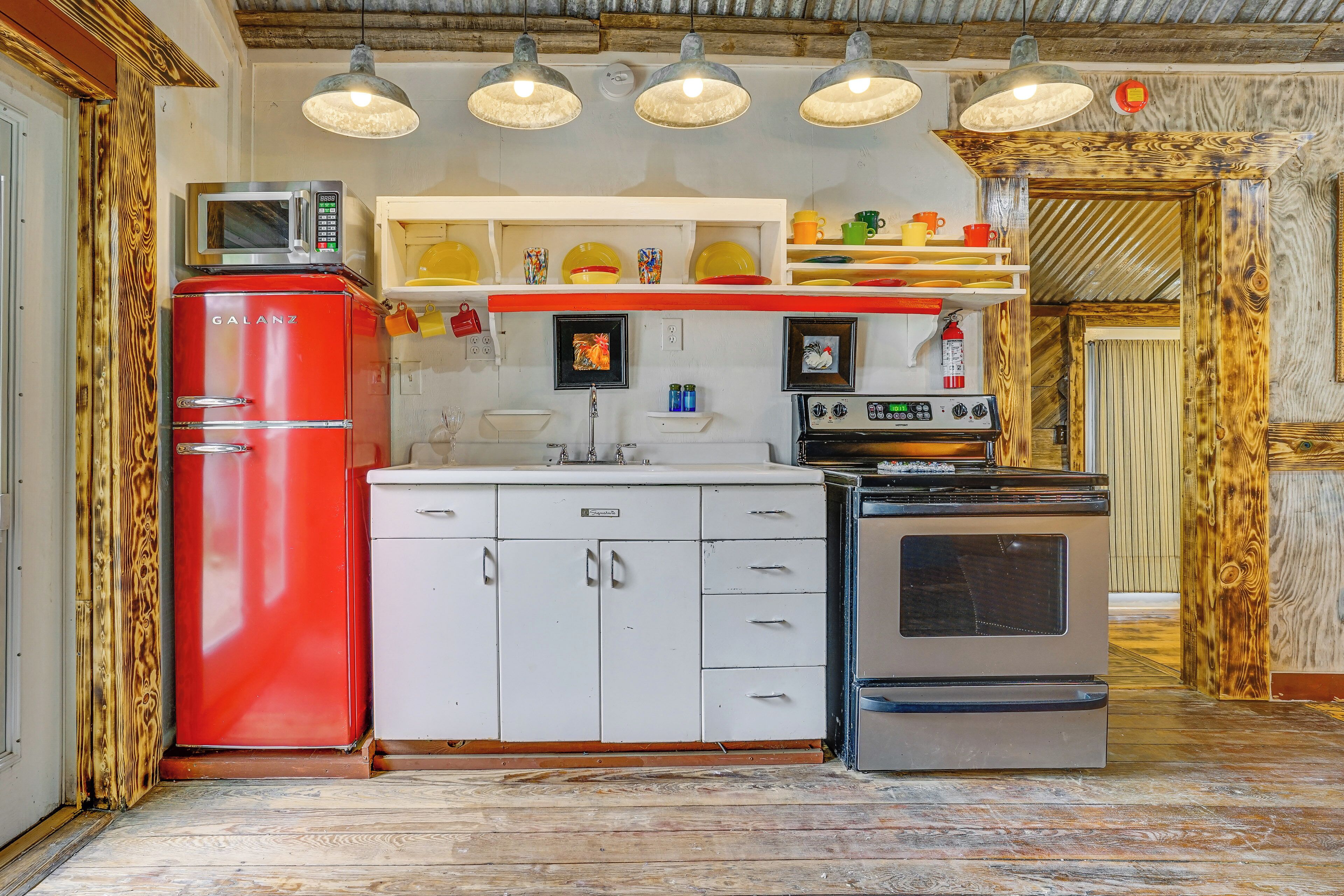 Une cuisine avec un réfrigérateur rouge, des armoires blanches, un évier et une cuisinière.