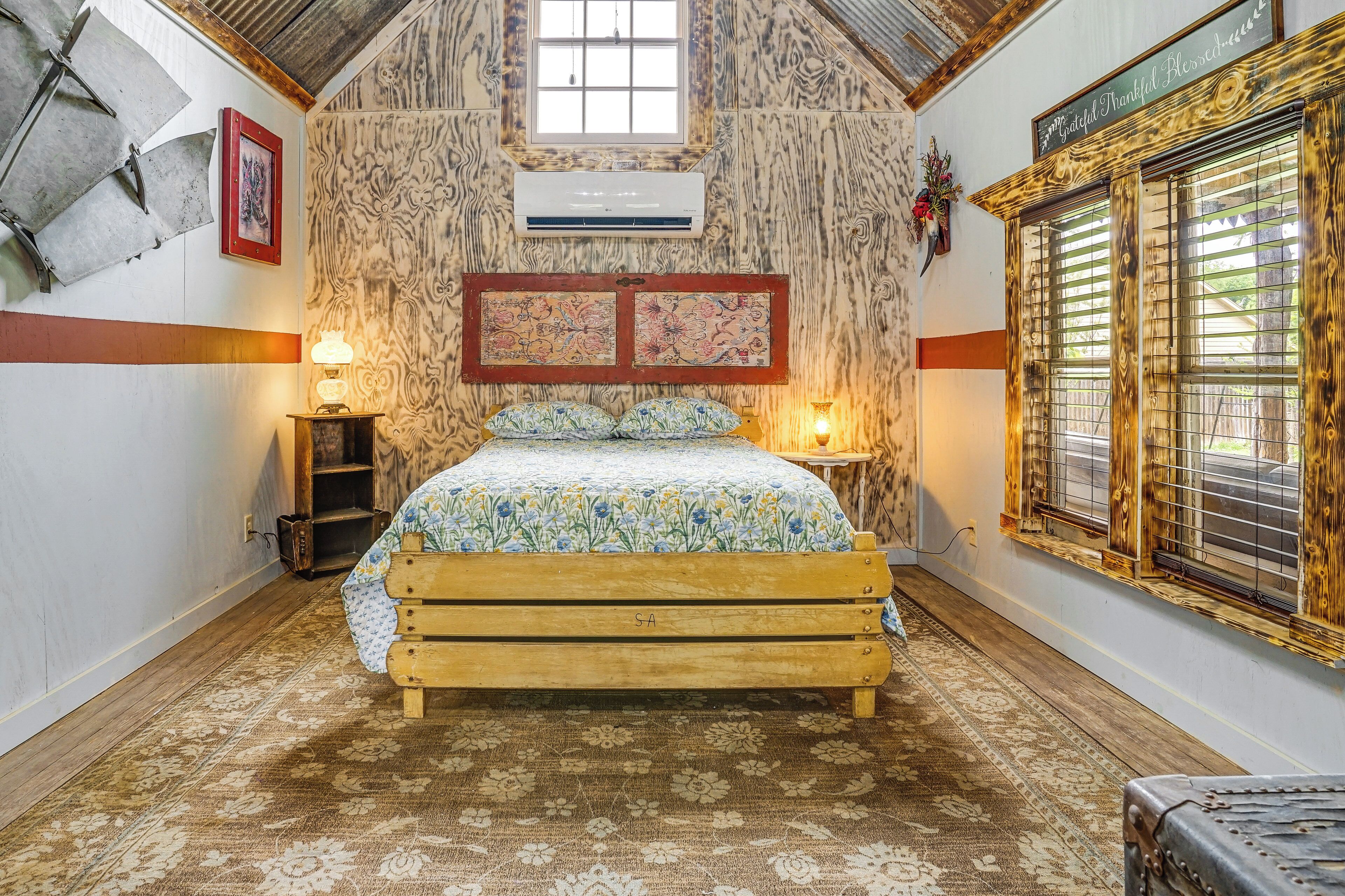 A bedroom with a wooden bed, patterned walls, a window with blinds, and a wall-mounted air conditioner.