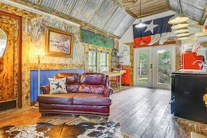 Une pièce avec un canapé en cuir, un tapis en peau de vache, un drapeau du Texas et un plafond rustique.