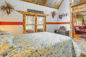 A bedroom with a floral bedspread, wooden doors, a red couch, and a decorative wall sign. - Walk to Granbury Square & Beach! 'texas Cottage' (Granbury)