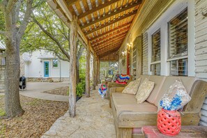 A covered porch with wooden beams, a bench, and a red basket with flowers.
