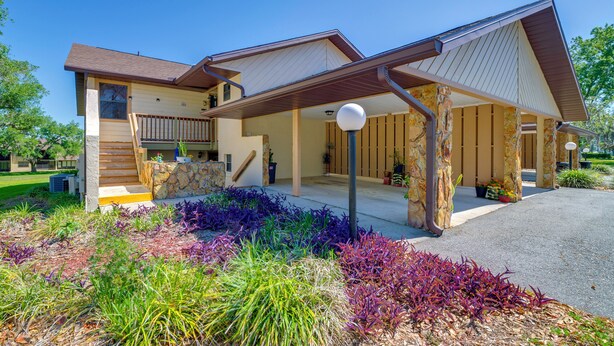 A two-story house with a covered porch, stone pillars, and a landscaped garden with various plants. - Relaxing Nature Coast Condo Near Crystal River (Hernando)