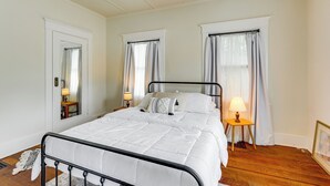 Un dormitorio con cama, dos mesitas de noche con lámparas, un espejo y una puerta.