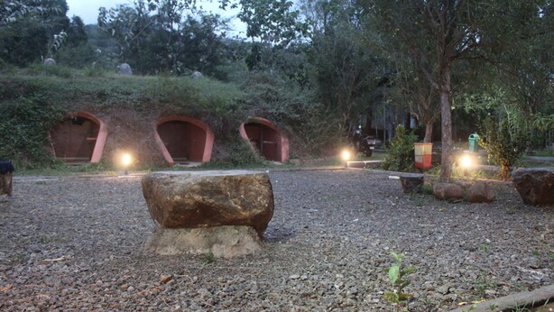 Un sendero de grava que conduce a estructuras escalonadas con luces, rodeado de árboles y rocas.