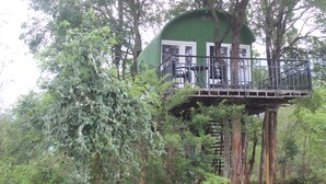 Una casa del árbol con balcón, rodeada de un bosque frondoso.