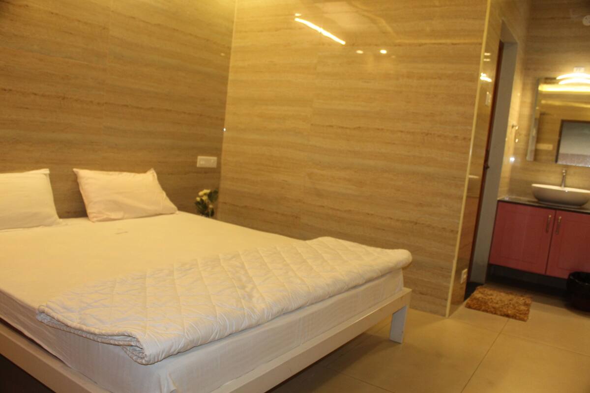 A modern bedroom with a large bed, a small bedside table, and a bathroom with a sink and mirror.