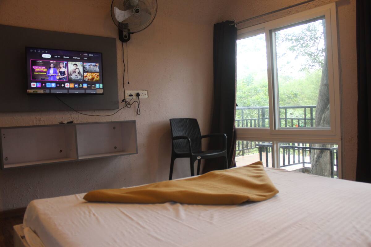 A hotel room with a bed, a TV mounted on the wall, a chair, and a balcony with a railing.