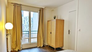 Un dormitorio con cama, armario, ventana con cortinas y lámpara.