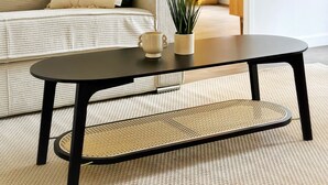 Un salón con sofá, mesa de centro, planta en maceta y puerta que da a otra habitación.