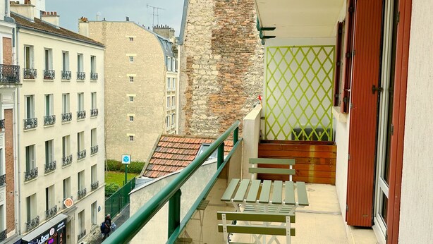 Un balcón con vista a la calle, una barandilla verde y un banco.