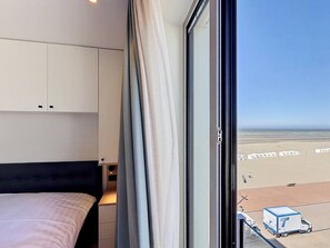 A hotel room with a bed, a window with curtains, and a view of the beach. - Flat Duin & Dijk - Koksijde (Koksijde)