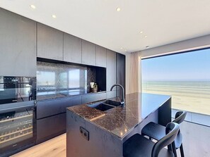 A modern kitchen with a marble countertop, stainless steel appliances, and a view of the beach. - Flat Duin & Dijk - Koksijde (Koksijde)
