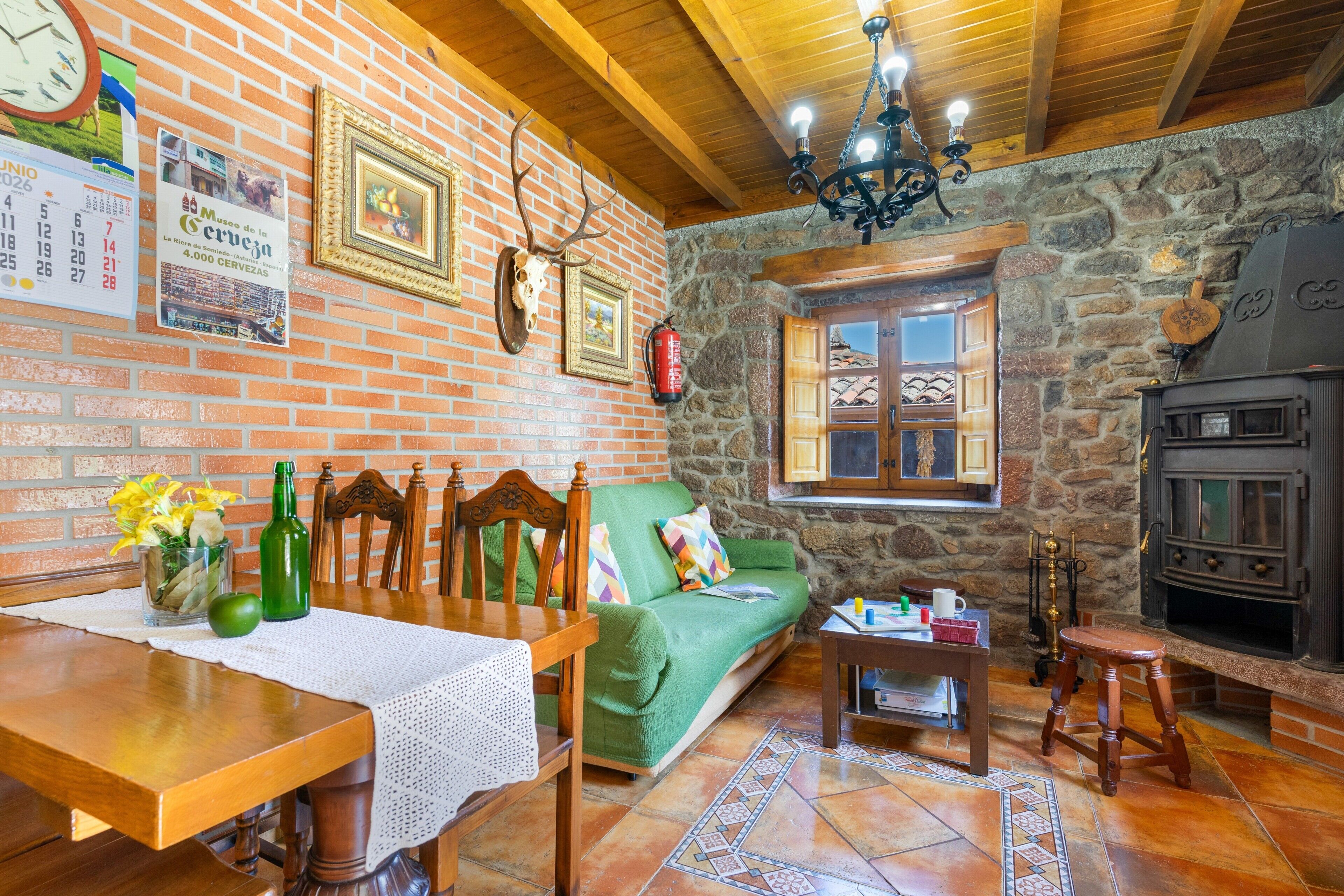 A rustic interior with a brick wall, wooden ceiling, a fireplace, a dining area with a table and chairs, and a green sofa.