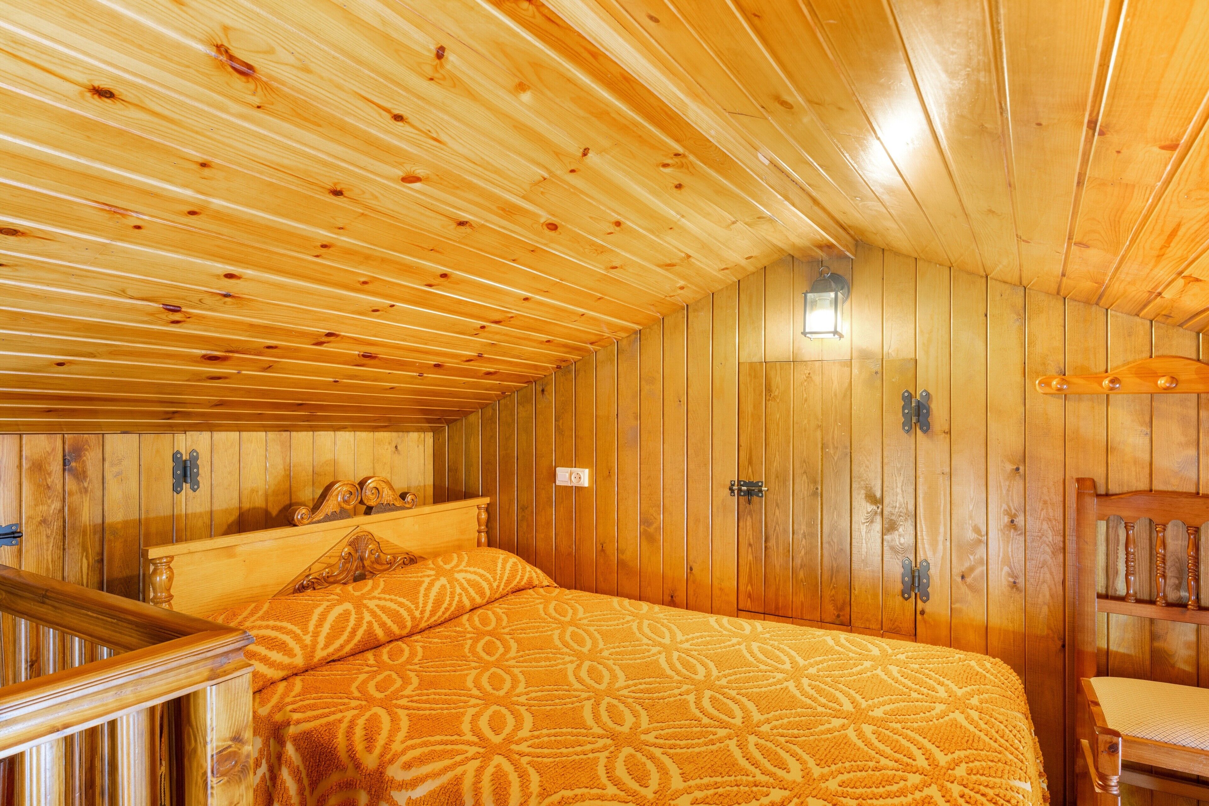 Um quarto de madeira com uma cama, uma cadeira e uma mesa pequena.