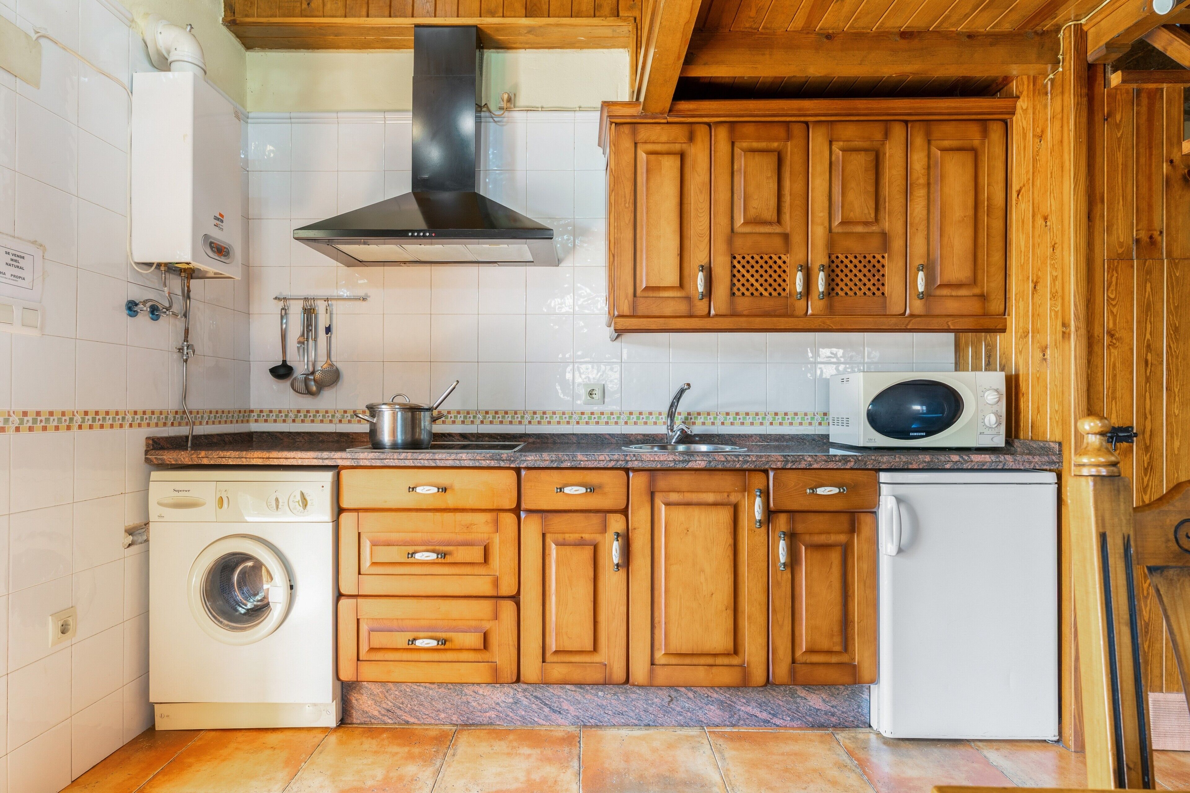 A kitchen with wooden cabinets, a built-in washing machine, a microwave, and a sink.